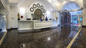 A reception area with a marble floor, a white reception desk, and a large clock above it.