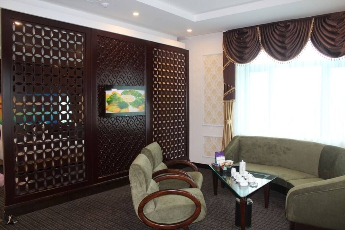 A hotel room with a large window, a sofa, two armchairs, a coffee table, and a decorative screen with a television.