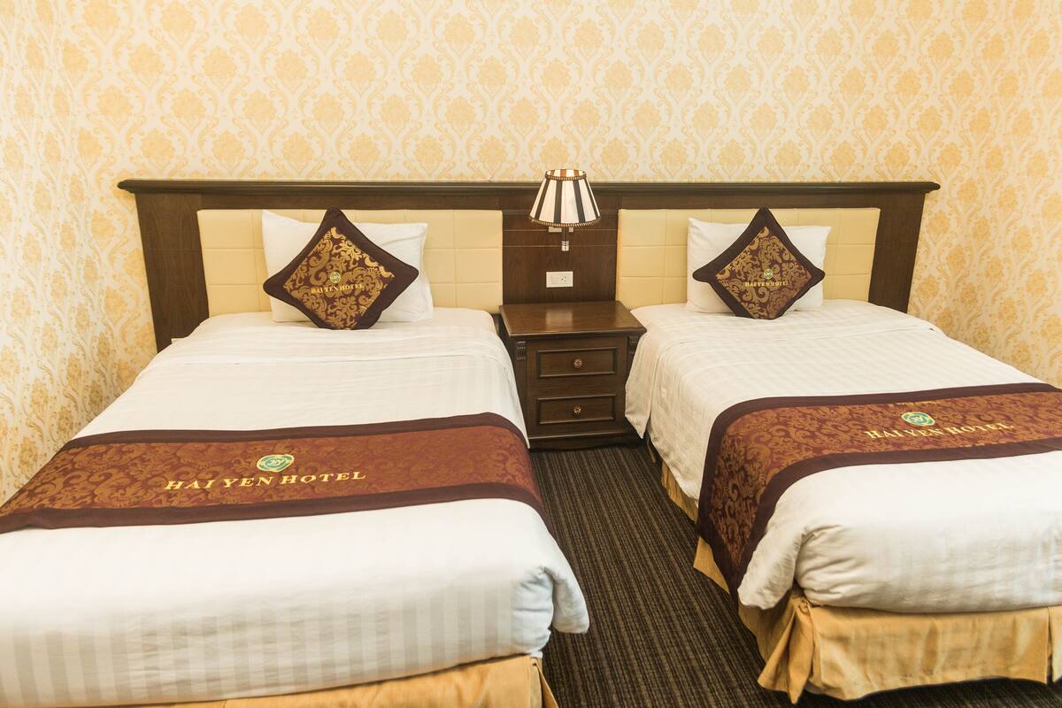 A hotel room with two beds, each with a headboard, a nightstand, and a lamp. The room has a carpeted floor and patterned wallpaper.