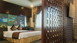 A hotel room with a large bed, a decorative headboard, a television, and a patterned wall. - Hai Yen Luxury Hotel (Cam Pha)