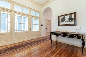 Una habitación con piso de madera, un amplio arco de entrada, una consola de madera oscura con cajones y un cuadro enmarcado en la pared.