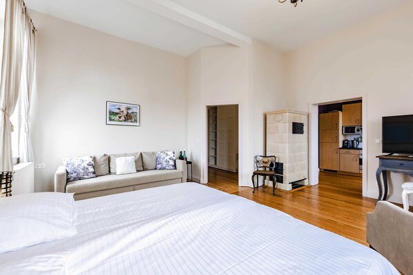 Un dormitorio con una cama grande, un sofá, un televisor y una kitchenette al fondo.