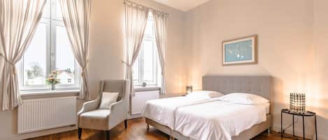 A bedroom with a bed, chair, bedside table, and a window with curtains.