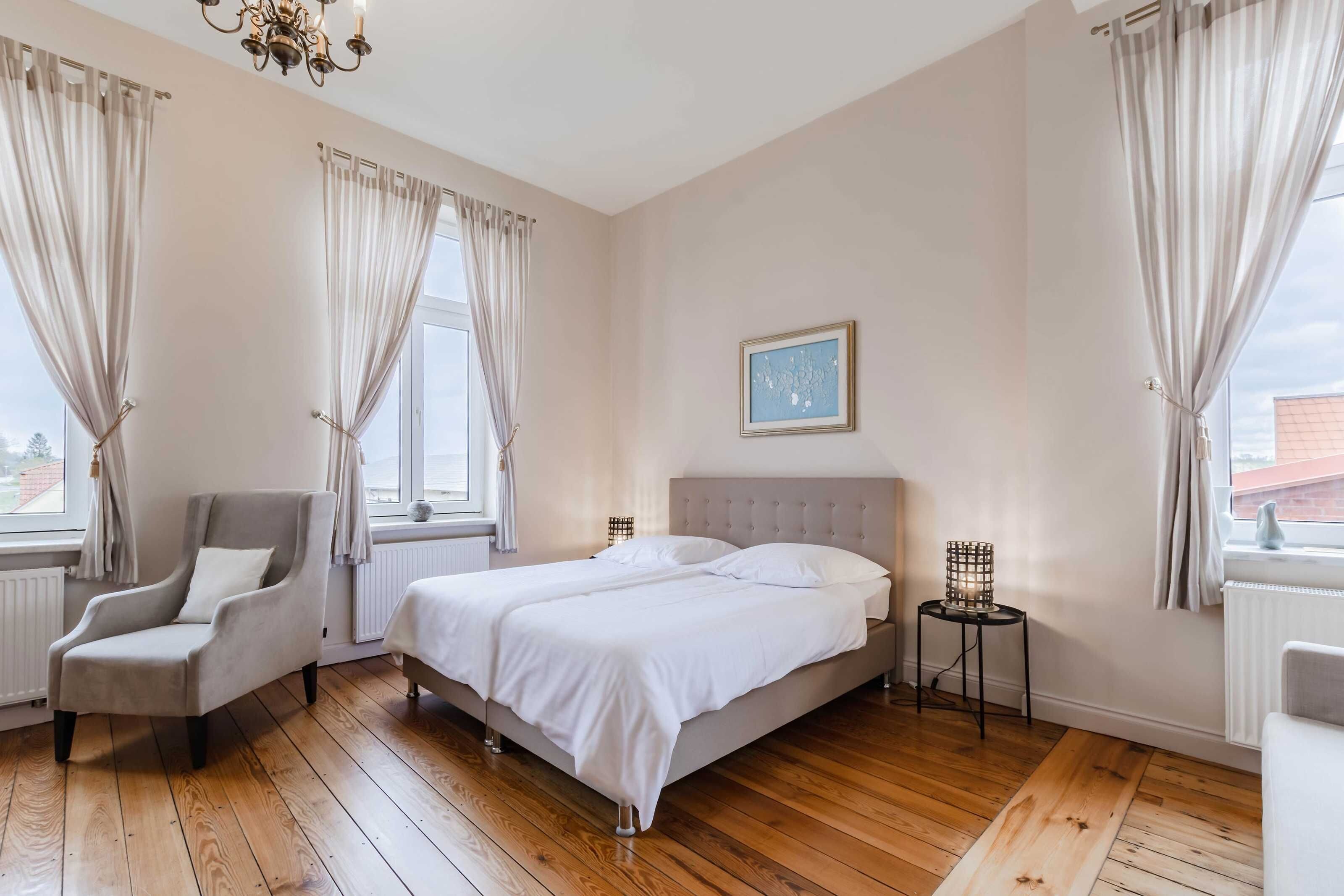 Een slaapkamer met een tweepersoonsbed, een stoel, een nachtkastje en een raam met gordijnen.