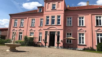 Ein rosafarbenes Gebäude mit vielen Fenstern, einem zentralen Eingang und Außenplätzen.