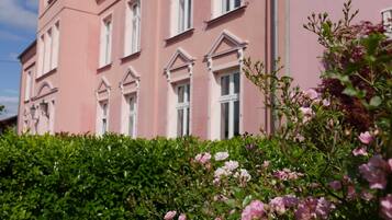 Ein rosafarbenes Gebäude mit vielen Fenstern und einem Hecken im Vordergrund.