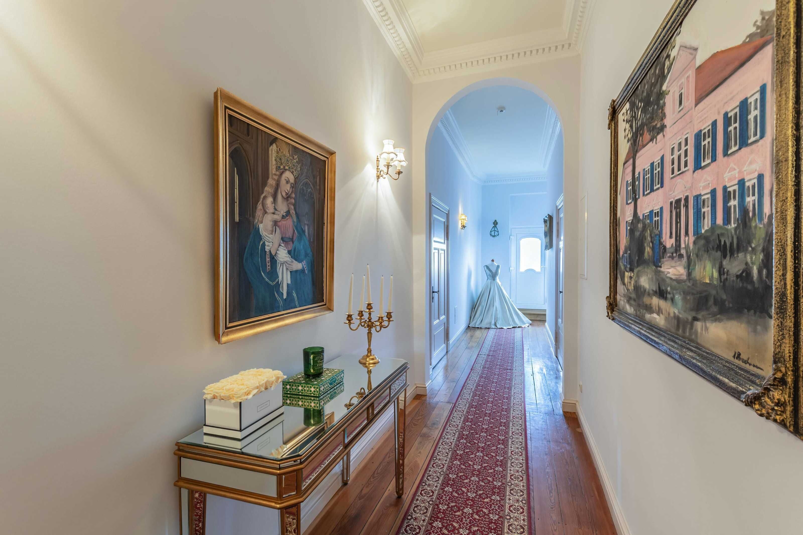 A hallway with a red carpet, a framed painting, a candelabra, and a mirror.