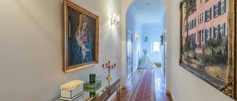 A hallway with a red carpet, a framed painting, a candelabra, and a mirror.