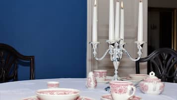 A table set with white and pink patterned tableware, a silver candelabra with lit candles, and dark wooden chairs.