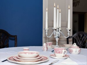Et bord dækket med hvidt og rosa service, en sølvstage med tændte lys og mørke træstole.