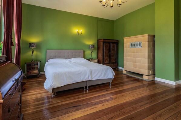 Une chambre à coucher avec un lit, un plancher en bois, des murs verts, une armoire et une table de chevet avec une lampe.