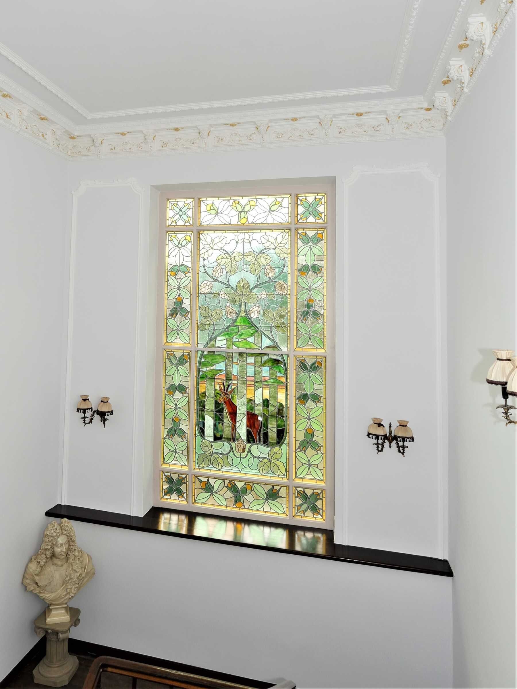 A room with a stained glass window, white walls, and a black bench.