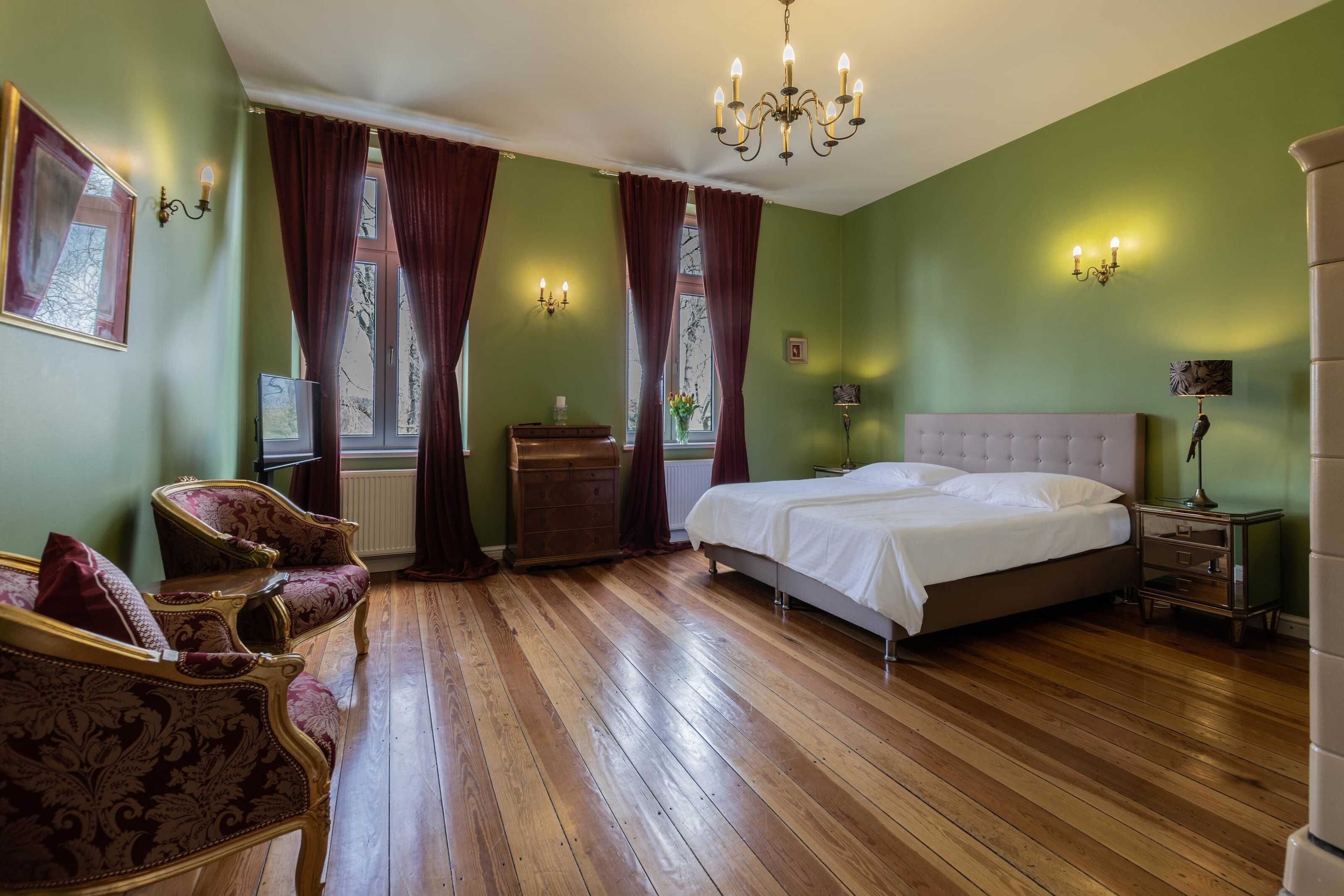 Ein Schlafzimmer mit einem großen Bett, einem Schminktisch, zwei Stühlen, einer Deckenleuchte und einem Fenster mit Vorhängen.