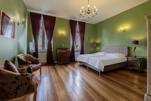 Un dormitorio con una cama grande, un aparador, dos sillas, una araña y una ventana con cortinas.