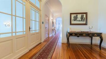 A hallway with wooden flooring, white doors, a red carpet, a dark wooden table with gold accents, and a framed picture on the wall.