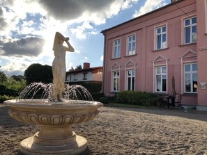 Eine klassische Statue auf einem Brunnen vor einem rosafarbenen Gebäude mit zahlreichen Fenstern.