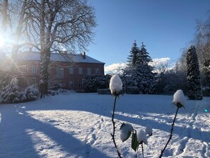 A snow-covered landscape with a red building, snow-covered trees, and a clear sky. - Zimmer Ludwigslust - Schlosshotel Groß Köthel (Hohen-Demzin)