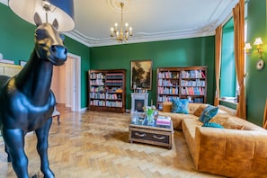 A room with a large horse statue, two bookshelves, a fireplace, a sofa, and a chandelier.