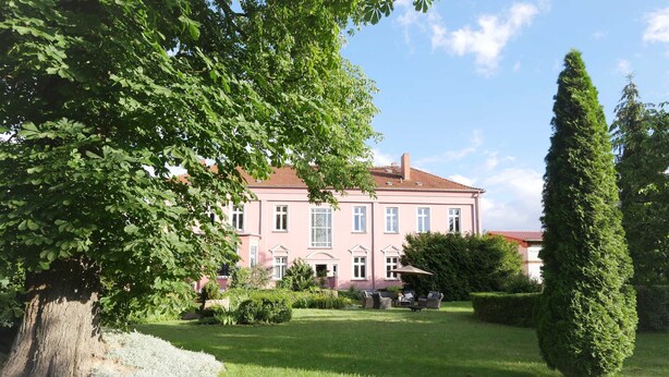 Een roze gebouw met een tuin en een hoge boom.