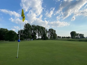 A golf course with a flag, trees, and a clear sky.