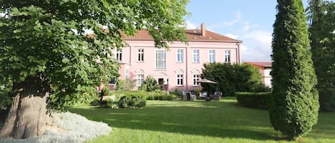 A pink building with a garden and a tall tree.