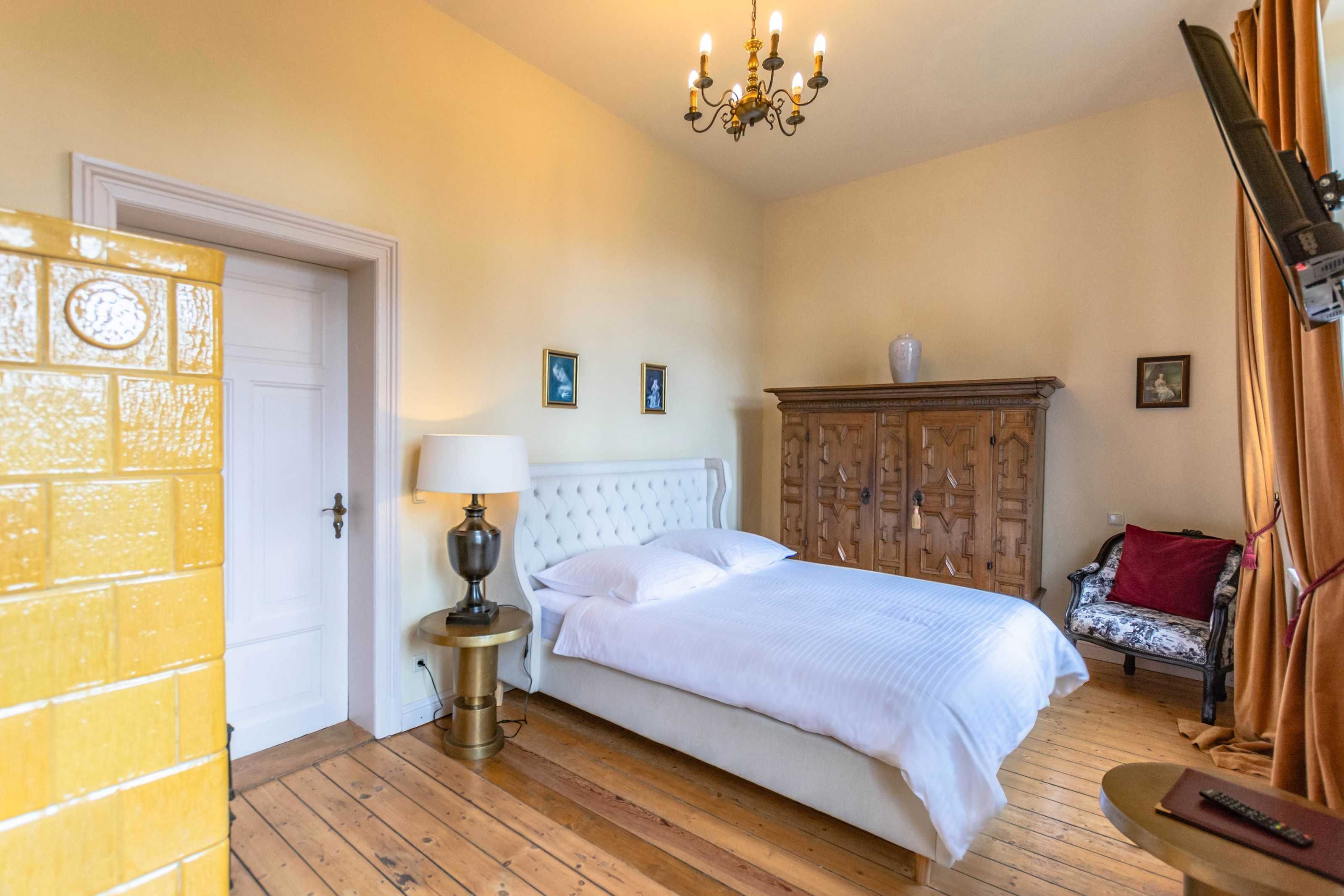 Ein Schlafzimmer mit Bett, Nachttisch, Holzschrank, Stuhl und einer Chandelüster.