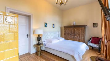 Ein Schlafzimmer mit Bett, Nachttisch, Holzschrank, Stuhl und einer Chandelüster.