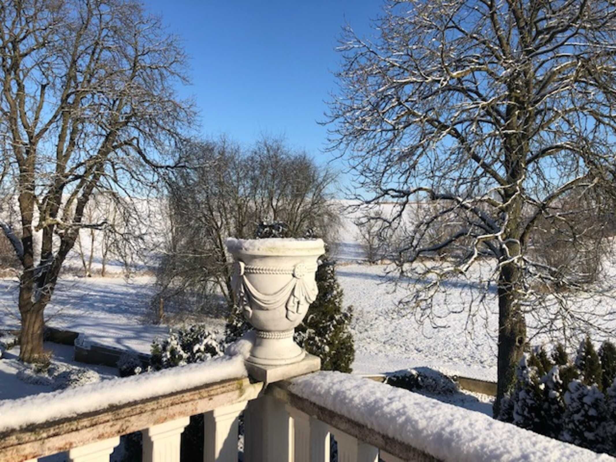 Un jardín cubierto de nieve con una urna blanca en un balcón.