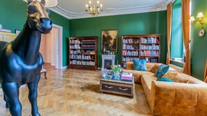 Ein Raum mit einer großen Pferdestatue, zwei Bücherregalen, einem Kamin, einer Couch und einer Kandelaber.