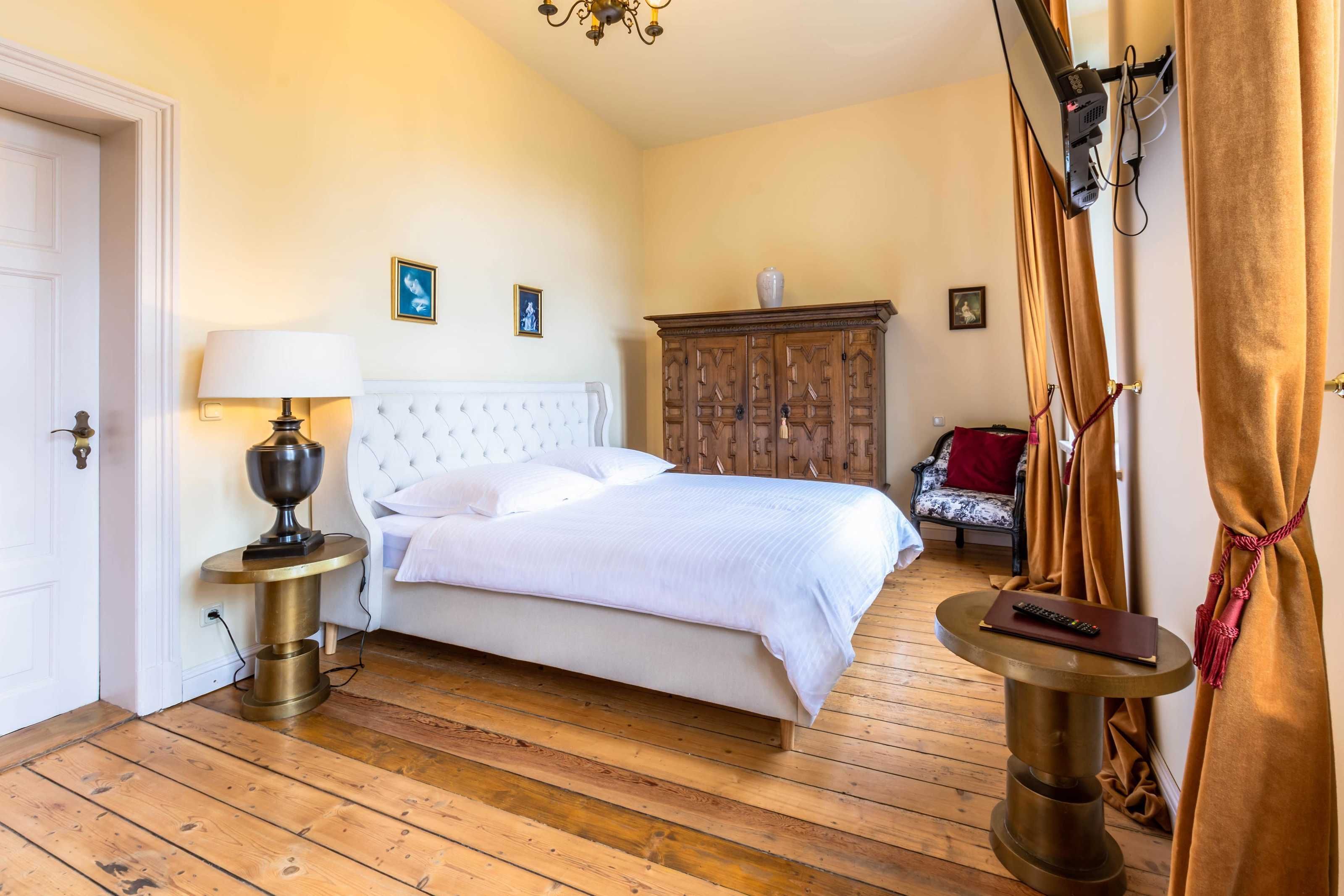 Een slaapkamer met een bed, bedlamp, houten vloer, kledingkast en een klein rond tafeltje met een afstandsbediening.