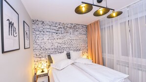 Ein ordentlich bezogenes Bett mit weißen Leinen, eine Wand mit Backsteinmuster und ein Nachttisch mit Lampe.