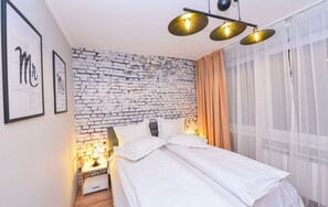 A neatly made bed with white linens, a brick-patterned wall, and a nightstand with a lamp. - Athene - 1 Bedroom Next to Victoria Avenue and Cismigiu Gardens (Bucharest)