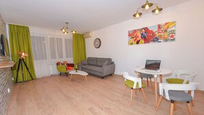 Ein modernes Wohnzimmer mit einem grauen Sofa, einem kleinen runden Tisch mit einem Laptop und einem farbenfrohen Kunstwerk an der Wand.