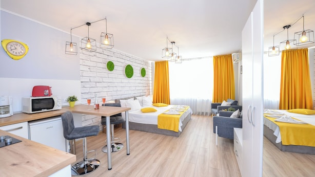 A modern hotel room with a kitchen area, a dining table, two beds, and a brick wall. - Candy Studio - Cismigiu Gardens - Quiet Room - Open Kitchen -smart Tv (Bucharest)
