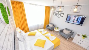 A modern hotel room with a large bed, a gray armchair, a small round table, and a TV on the wall. - Candy Studio - Cismigiu Gardens - Quiet Room - Open Kitchen -smart Tv (Bucharest)