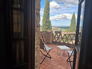Une porte ouverte donnant sur un patio dâoĂč lâon peut admirer des collines verdoyantes, ainsi que deux chaises et une petite table.