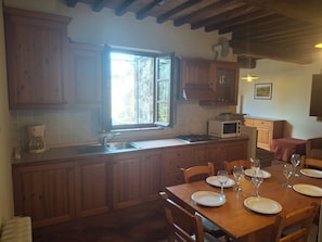 Une cuisine avec des meubles en bois, une fenĂȘtre, un four Ă micro-ondes et une table Ă manger pour quatre personnes.