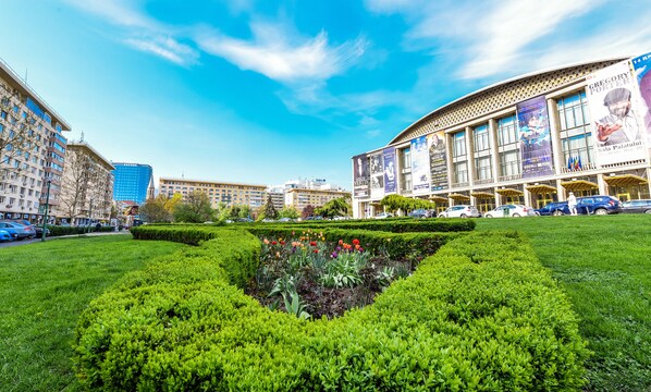 Una plaza urbana con un jardín central, rodeada de edificios de varios pisos, incluyendo un gran edificio con fachada curva y varios anuncios.