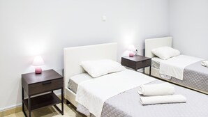 Een hotelkamer met twee eenpersoonsbedden, elk met een witte hoofdbord en een klein nachtkastje met een lamp.