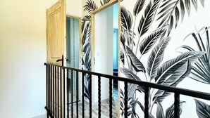 A staircase with a black railing, a wooden door, and a wall with a tropical leaf pattern. - Campo Vecchio DRACENA (Ghisonaccia)