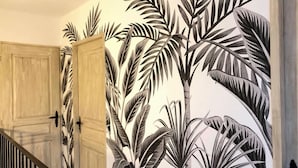 A hallway with a large wall mural of tropical foliage, a wooden door, and a staircase. - Campo Vecchio DRACENA (Ghisonaccia)