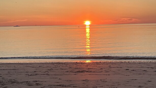 Een strand met een ondergaande zon boven de oceaan.