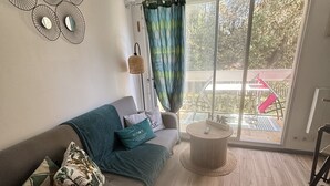 Een moderne woonkamer met een grijze bank, een ronde salontafel en uitzicht door een glazen deur op een terras.