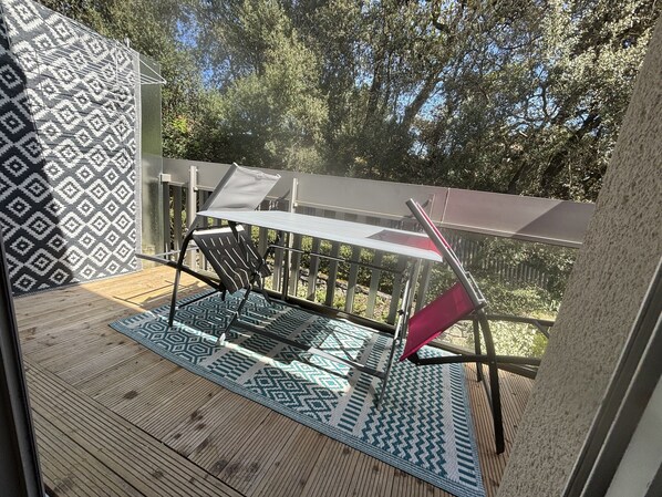 Una terraza de madera con un tapete estampado, una mesa con sillas y vistas a árboles.