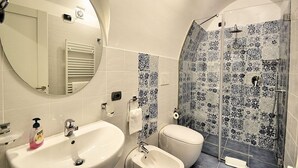 Un baño con espejo redondo, lavamanos, bidé y ducha con azulejos de diseño azulado.