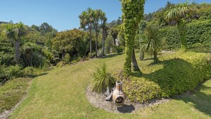 Un jardin luxuriant, avec une grande variété d’arbres et d’arbustes, un sentier sinueux et un pot décoratif.