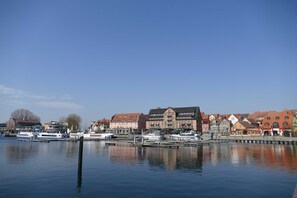 A waterfront with boats docked, buildings with red roofs, and a clear blue sky.