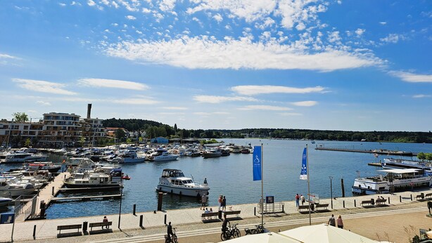 Ein Yachthafen mit vertäuten Booten, ein klarer Himmel und eine Uferpromenade.