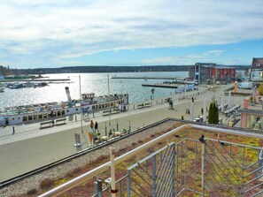 A waterfront promenade with a dock, boats, and a building with a red facade.