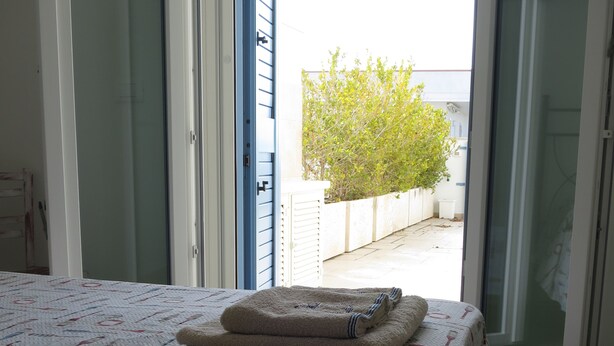 A bedroom with a bed, a window with a view of a tree, and a door. - SeaHouse (Torre Vado marina di morciano di leuca)